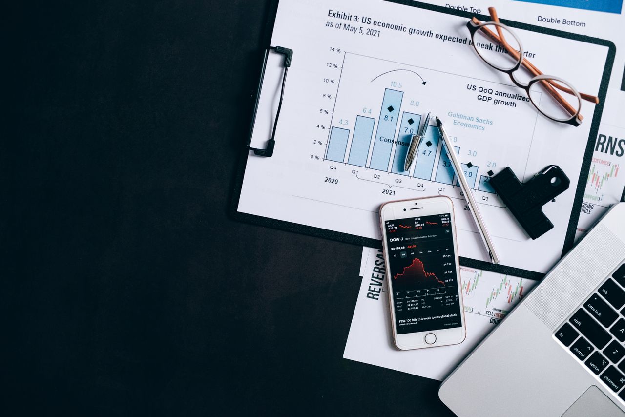 Top view of financial reports, smartphone showing stock market data, and a laptop on desk.